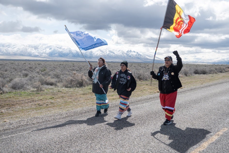 Three indigenous women carrying flags on a rural road