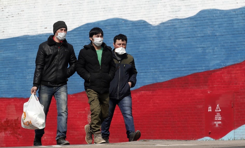 Three men in face masks walk in front of a mural of the Russian flag