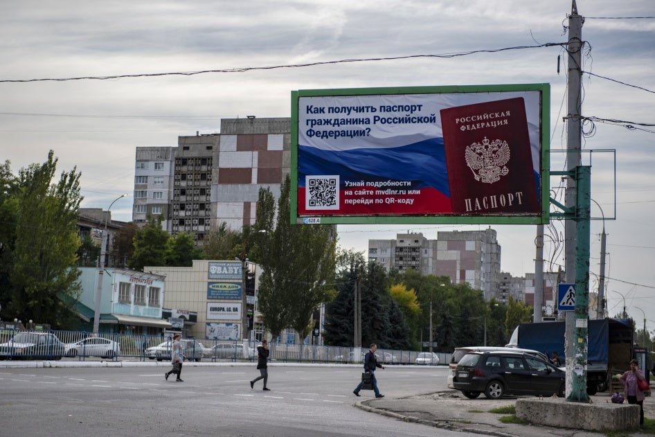 People cross a street with a billboard reading "How to get a passport of a citizen of Russia" in the occupied territory of Luhansk, September 22, 2022.