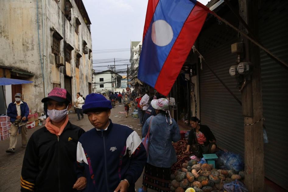 Lao people walk past their country flag, in the capital Vientiane, Laos. 