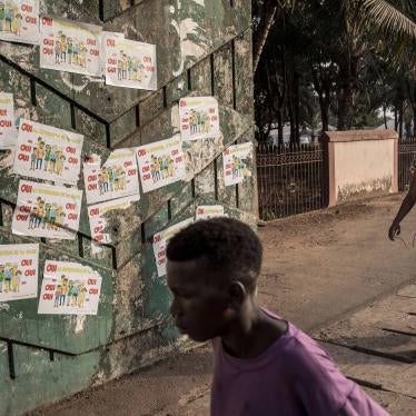 Two people walk down a street in front of a wall covered in political posters