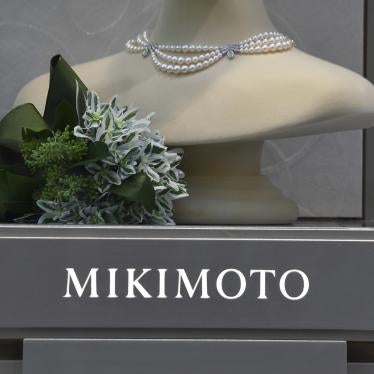 A pearl necklace is displayed over a gray sign that reads "Mikimoto"