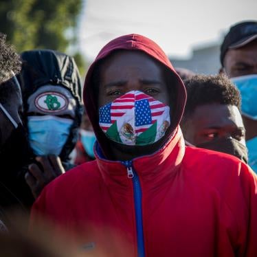 A migrant from Haiti wearing a mask in the colors of the Mexican and US flags stands at a border crossing with others, waiting to asylum in the US, February 19, 2021. 