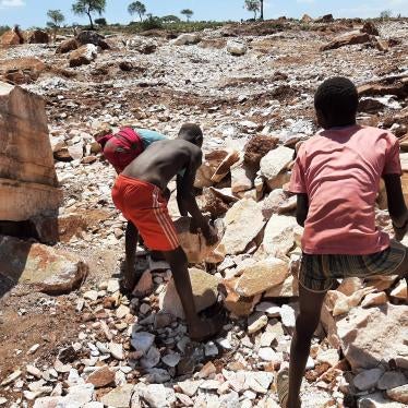 Two boys pick up large rocks at a quarry 