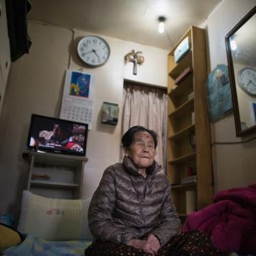 An elderly woman seated on the floor of an apartment