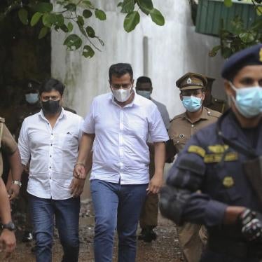 Two Sri Lankan parliamentarians walk to prison bus escorted by officers.