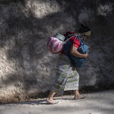 A woman transports water on her back while carrying her youngest son in her arms