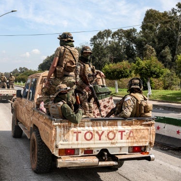 Uniformed and armed soldiers ride in the back of a truck
