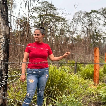 A woman stands in the forest with her hand on a wire fence.